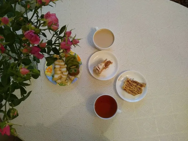 Desayuno para dos personas con té y pasteles con rosas en un jarrón —  Fotos de Stock