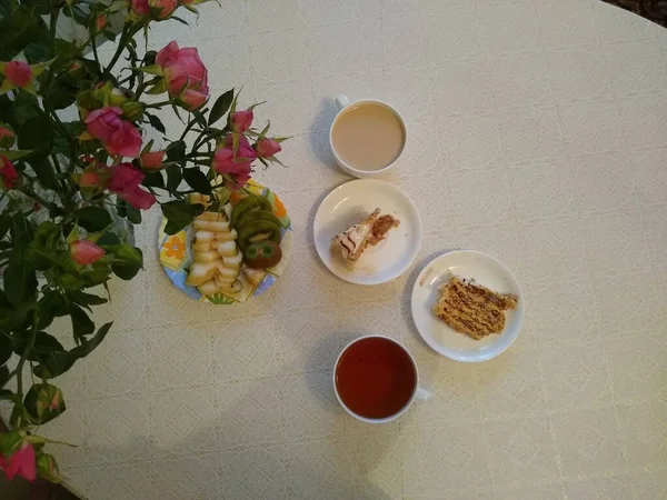 Café da manhã para dois com chá e bolos com rosas em um vaso Imagem De Stock