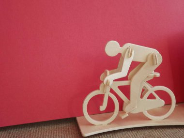 Pembe arka planda tahtadan yapılmış bisiklete binen bisikletçi.