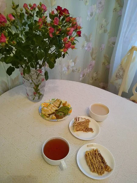 Desayuno para dos personas con té y pasteles con rosas en un jarrón — Foto de Stock