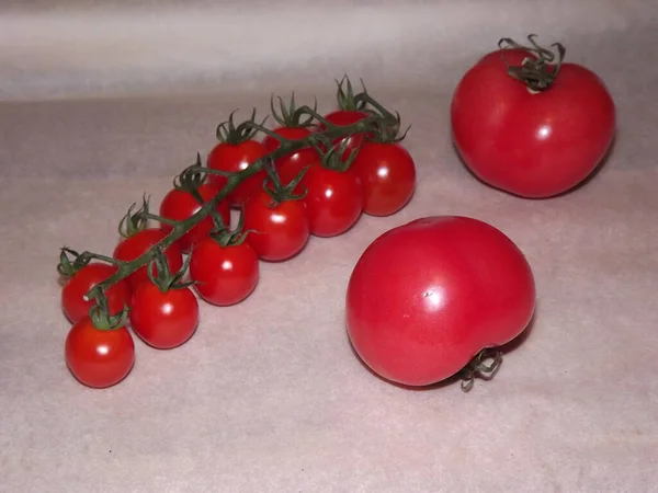 Dos tomates grandes y tomates cherry en las ramas se cierran sobre un fondo beige — Foto de Stock