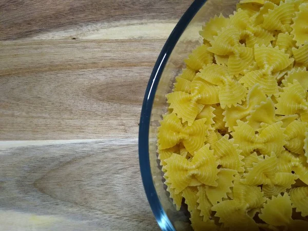 Pasta in Form von Schleifen in einem Glasbehälter auf einem hölzernen Hintergrund — Stockfoto