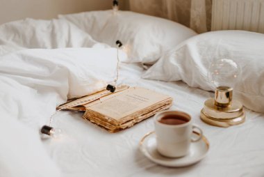 Kahve ve kitap beyaz yatakta.