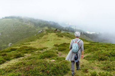 Sisli bir günde sırtında sırt çantasıyla dağda yürüyen yaşlı bir yürüyüşçü..