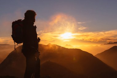 Yürüyüşçü gün batımında bir dağın tepesinden gün batımını izliyor..