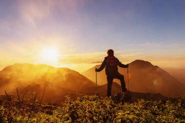 Sırt çantalı dağcı ve yürüyüş direkleriyle gün batımında dağda zirve yapıyor. Llanes Dağları, Asturias, İspanya. 