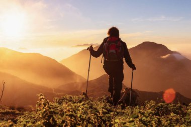 Sırt çantalı ve yürüyüş direkleriyle geri dönen yürüyüşçü dağlardan gün batımını izliyor. Llanes Dağları, Asturias, İspanya.