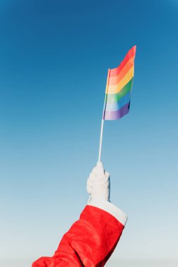 Noel Baba elinde arkasında açık mavi gökyüzü olan bir lgbt gurur bayrağı tutuyor. Kapsayıcı Noel.