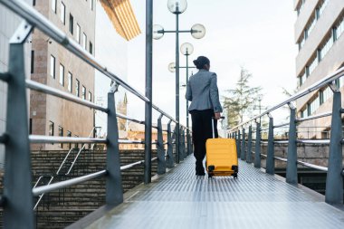 Sırtüstü uzanmış, sarı bavullu bir kadın sokakta metal bir podyumda yürüyor. iş gezisi konsepti.