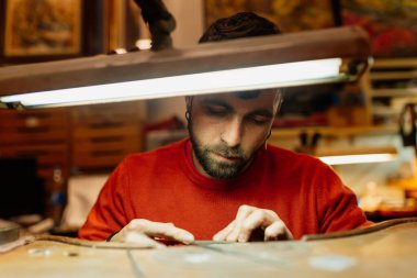 Kuyumcu adam tezgahındaki bir mücevhere dikkat ederek çalışıyor.