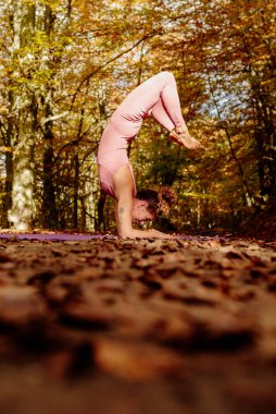 Latin kadın ormanda yoga dengesi uyguluyor, vrischikasana egzersizi yapıyor, akrep pozu veriyor..