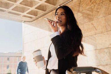 İspanyol iş kadını iş yerinde bir mola sırasında sesli mesaj göndermek için akıllı telefonunu kullanıyor.