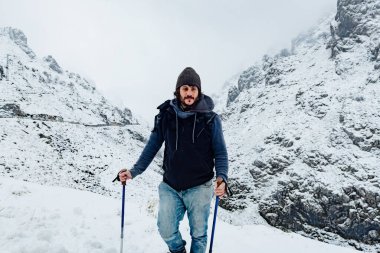 Karlı bir dağ manzarasında yürüyüş yapan bir adam.