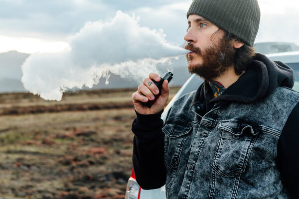 middle-aged white man with beard and tattoos giving off clouds of steam after vaping with his electronic cigarette.