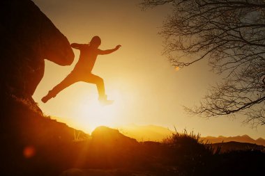 Gün batımında dağlarda yürüyüş yaparken bir dağın kayaları arasında zıplayan insan silueti. sağlıklı yaşam tarzı