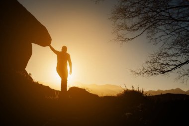 Gün batımında dağda bir kayanın yanında zirve yapan insan silüeti. sağlıklı yaşam tarzı.