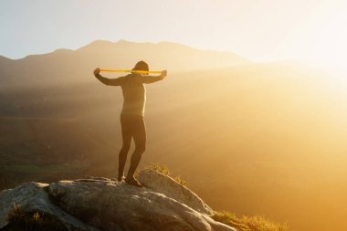 Gün batımında dağın tepesinde vücut geliştirmek için elastik bant kullanan bir adam. fitness ve sağlıklı yaşam tarzı.