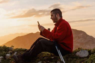 Yürüyüş günü boyunca dağlarda cep telefonu kullanan bir adam oturuyor. Açık hava aktiviteleri. iletişim.