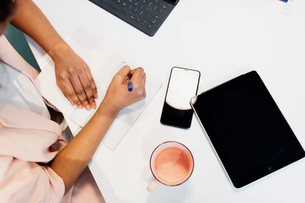 Ofis masasında çalışan tanınmayan Afrikalı kadınların el yazısıyla yazılmış notları akıllı bir telefon ve tabletle birlikte masanın üzerine koydukları resimlerin en üst görüntüsü..