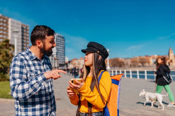 white male giving direction to a young asian female tourist in a european city. Chinese girl doing tourism in Gijon, Asturias, Spain