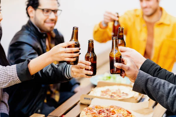 multiracial group of friends toasting with beer in a restaurant while eating pizza after work