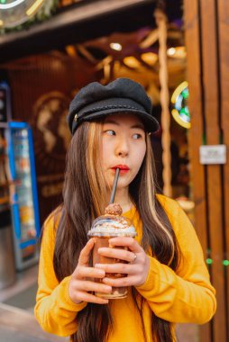 Genç Asyalı kadın pipetle içiyor. Çikolatalı ve kremalı özel bir kahve..