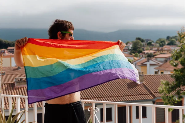 白い男が家のテラスでLgbtの誇りの虹の旗を振っている 家にいる本当の人たちは — ストック写真