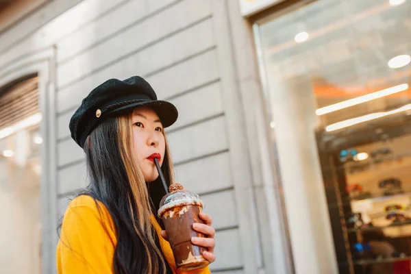 young asian girl enjoying a chocolate milkshake while walking around the city.