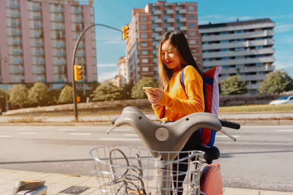 young asian girl using an app from her smartphone to rent a bike for urban mobility. sustainable cities.