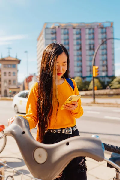 young asian woman using an app on her smartphone to pay for a bike rental for urban mobility. sustainable cities and ecological transport.