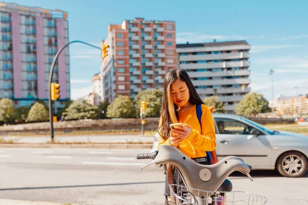 young asian woman using an app on her smartphone to pay for a bike rental for urban mobility. sustainable cities and ecological transport.