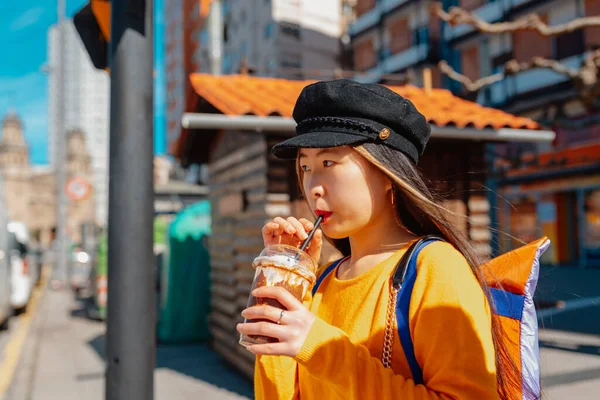 young asian woman having a chocolate milkshake with coffee while walking in a city