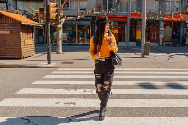 young asian woman crossing a crosswalk while drinking a chocolate milkshake and sightseeing in a european city.