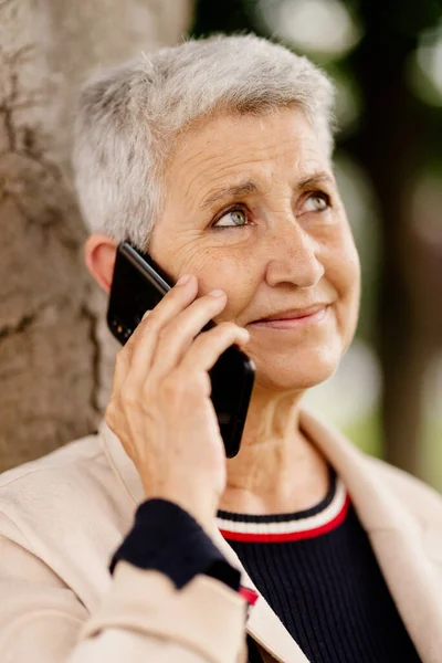 natural portrait of an older woman with gray hair, with a serene and happy using her mobile phone.