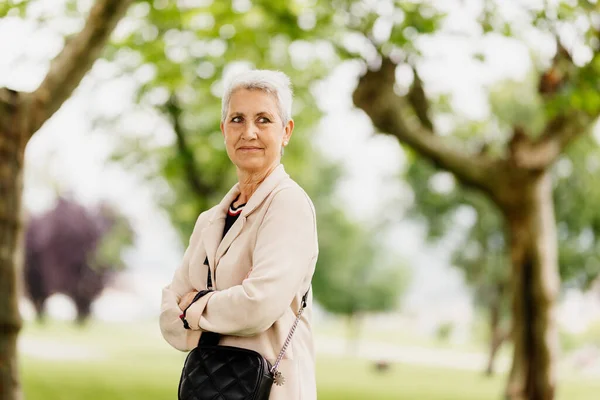 natural portrait of older woman with crossed arms and gray hair, with serene and happy gesture looking at infinity in a park.