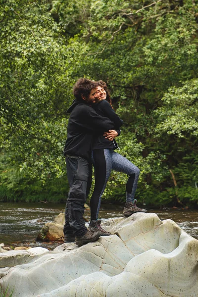hiker couple hugging on a rock over a river in the forest
