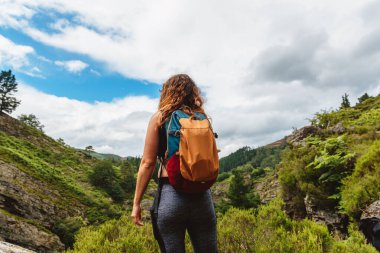 Sırt çantalı bir kadın, bir günlük yürüyüş sırasında ormanı ve dağ manzarasını inceliyor. hafta sonu açık hava aktiviteleri kavramı