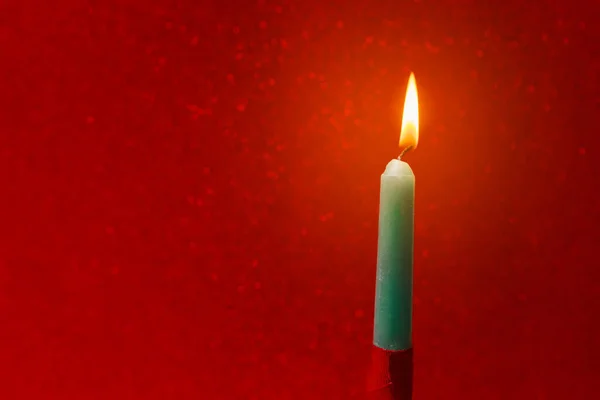 christmas postcard with burning green and red candle in front of a bright red background with glitter