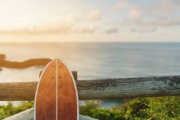 スケートボード サーフィンスケートやロングボードスケート 海と夕日の前にビーチと木製の手すりにもたれています アウトドアと夏のスポーツのコンセプト — ストック写真