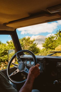 Tanımlanamayan insanların elleri, direksiyon tutarken, arazi arabasıyla dağ yolunda araba sürerken. seyahat ve macera. Etkin turizm.