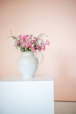 Östomalı buket, beyaz vazoda yaz çiçekleri, pembe-bej arka planda..