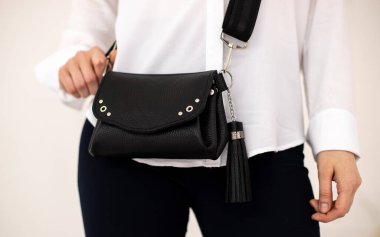 Siyah pantolonlu bir kız ve omzunda el çantası olan beyaz bir bluz..