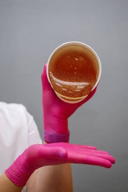 Kırmızı lastik eldivenli bir kız tüy dökmek için balmumu döker..