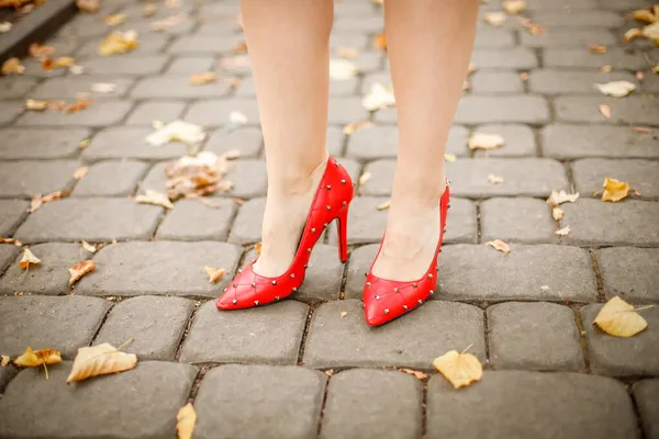 Női lábak piros cipőben egy kő járdán — Stock Fotó