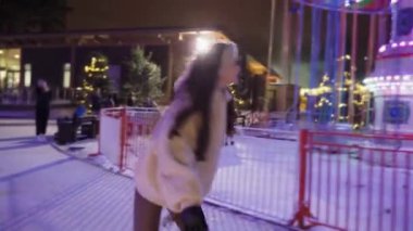 Atlıkarıncanın neon ışıklarının arka planında buz pateni yapan genç bir kız. Yüksek kalite 4k görüntü