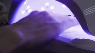 Kız, ellerini kuaförde ultraviyole lambanın altında kurutmak için koyuyor. Yüksek kalite 4k görüntü