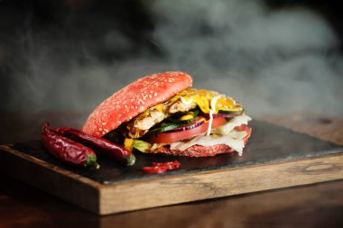 Ahşap bir tahtanın üzerinde kırmızı baharatlı burger ve arka planda duman. Yüksek kalite fotoğraf