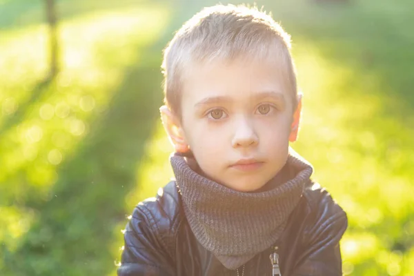 Retrato emocional de un niño en edad preescolar. Caucásico niño mirando en cámara contra luz verde fondo al aire libre al atardecer. — Foto de Stock