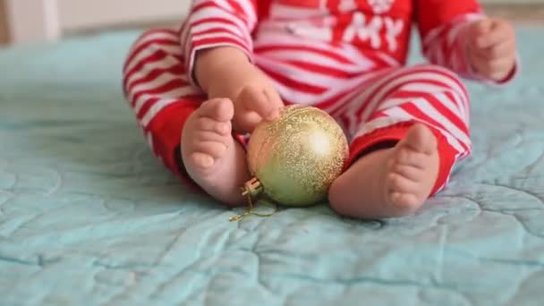 一个穿着圣诞服装的小宝宝手里拿着一个金色的圣诞舞会。新年及寒假概念 — 图库视频影像