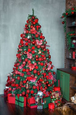 Kırmızı ve yeşil toplarla süslenmiş Noel ağacı, karanlık bir iç mekânda oyuncaklar ve süsler. Hediyeler ve parlak kutularla süslenmiş yeni yıl ağacı. Dikey çekim.